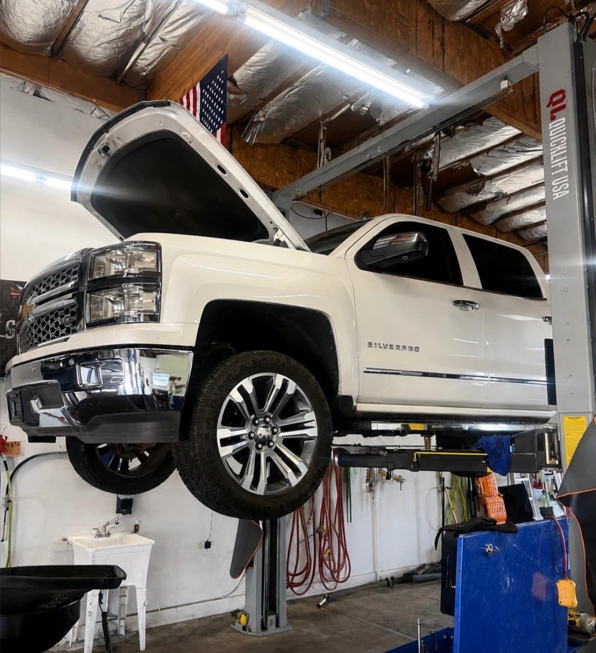 A Chevrolet Silverado up on the two-post lift with its hood open at Mesa Auto & Fleet in Mesa, Arizona